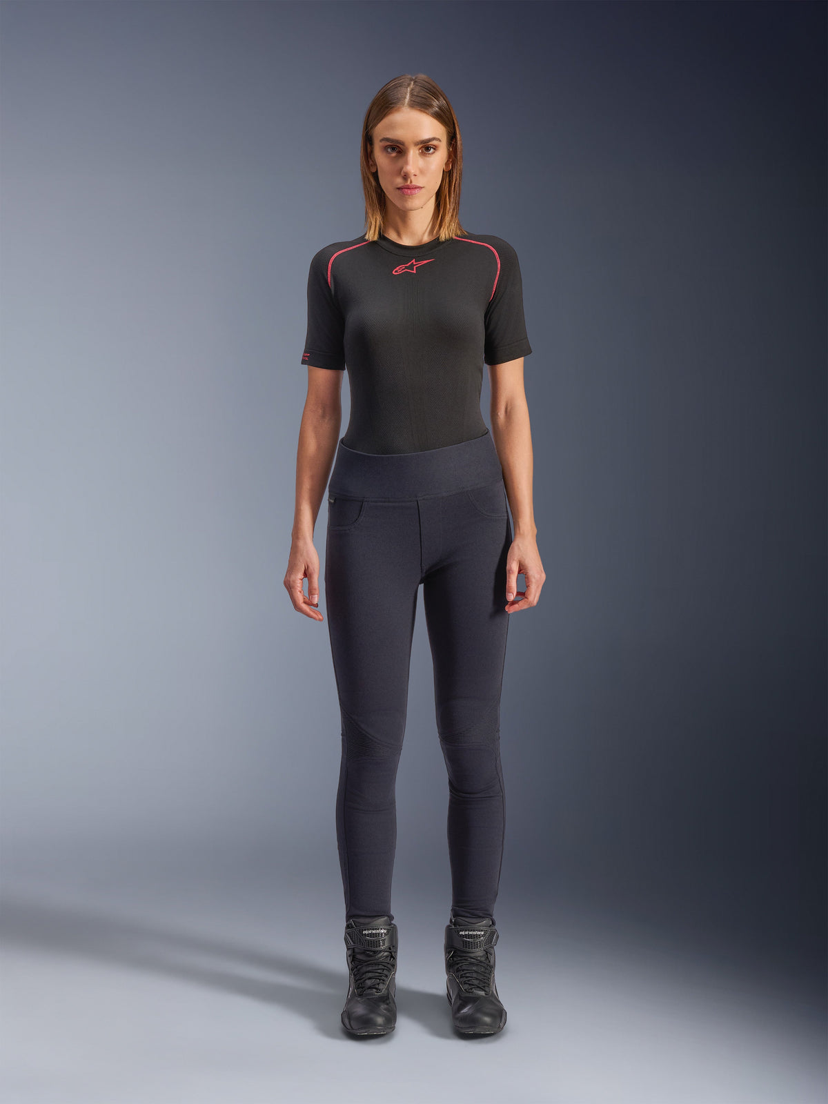 Alpinestars Stella Flex-AST Leggings, women's urban motorcycle leggings in Black, skinny high-waisted design worn with a black short-sleeve technical top and black riding boots, featuring accordion knee panels and a contemporary minimalist look