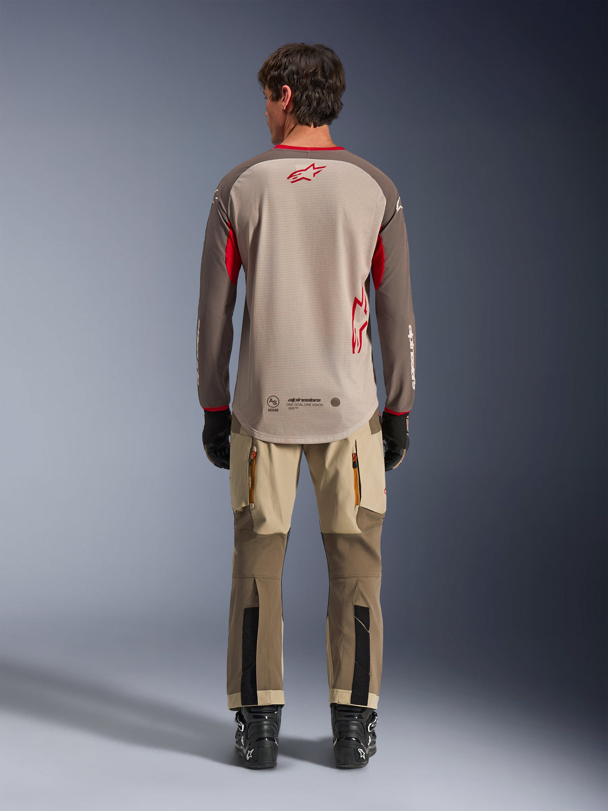 Alpinestars Maxdura Dual Jersey in Aluminum Walnut, back view, tan mesh torso with brown sleeves and red logos, dropped rear hem, paired with adventure riding pants and black boots.