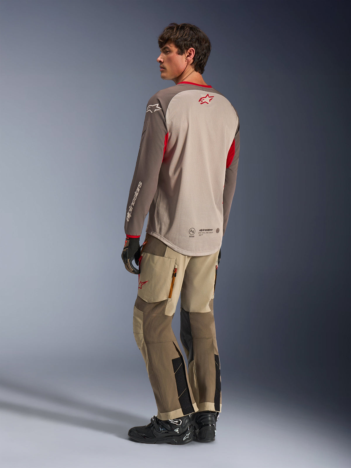 Alpinestars Maxdura Dual Jersey in Aluminum Walnut, back view of adventure motorcycle jersey featuring a breathable mesh torso and red accents, paired with matching technical adventure pants and black boots
