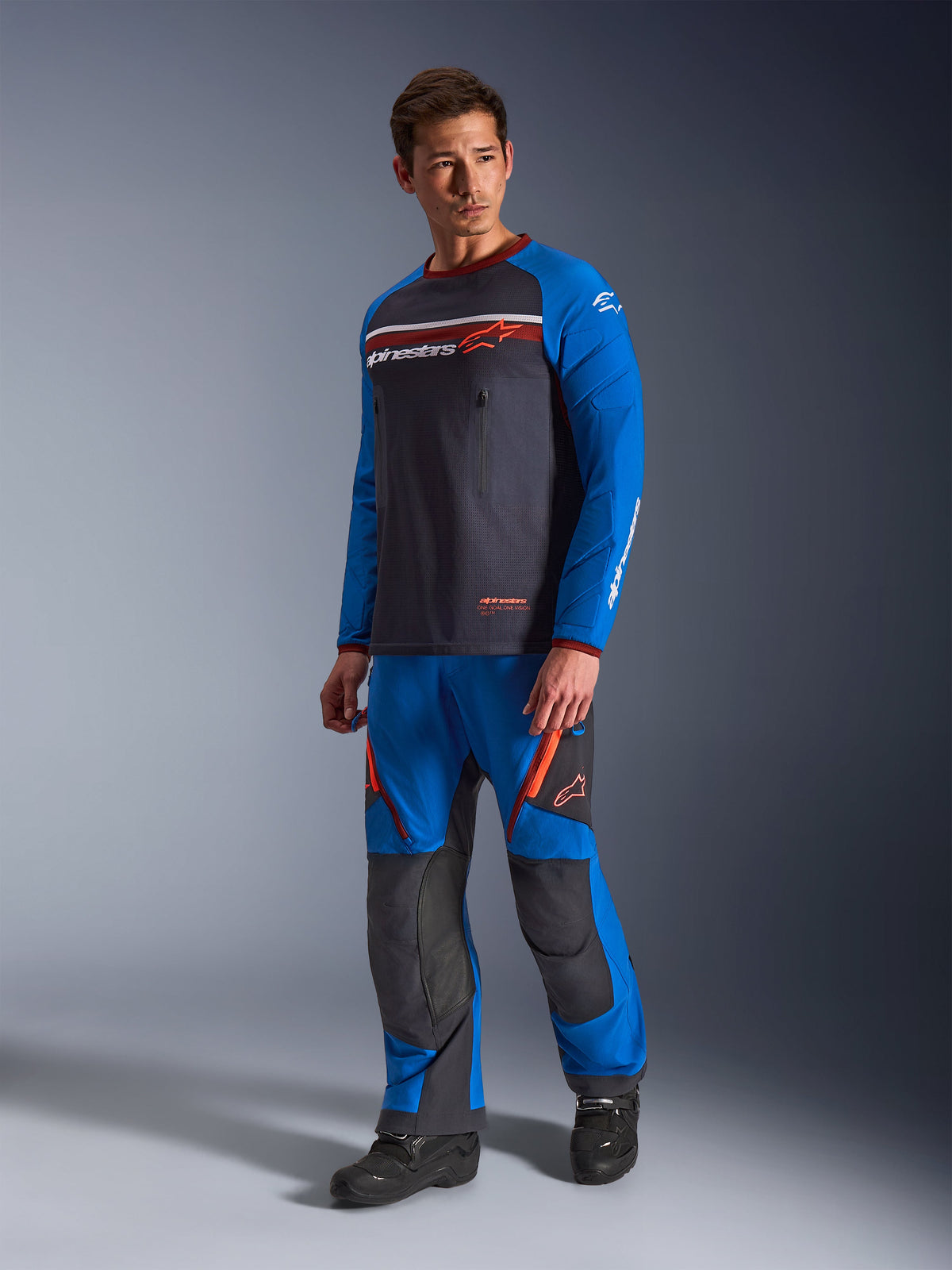 Alpinestars Maxdura Dual Jersey, Deep Gray and Royal Blue, adventure motorcycle jersey with a mesh torso and royal blue sleeves, worn by a model with matching off-road riding pants, featuring zippered chest pockets and Alpinestars branding.