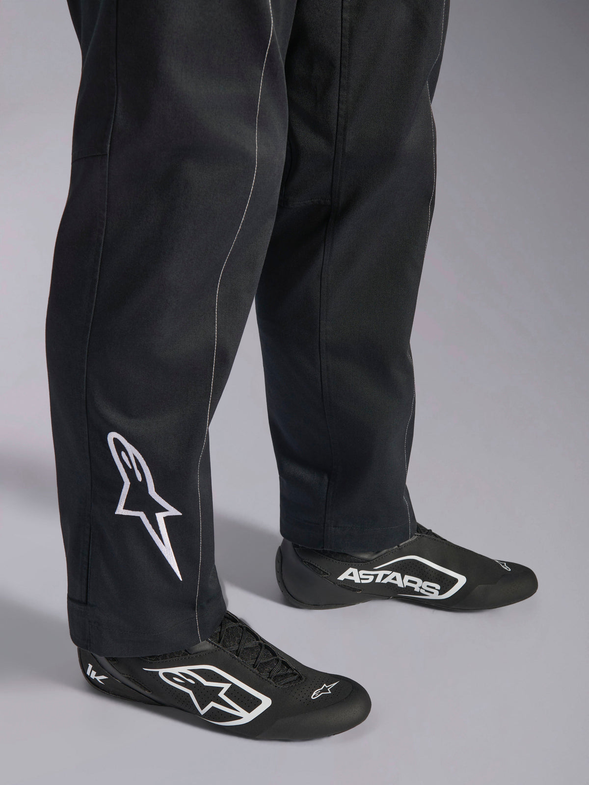 Alpinestars Kart Indoor V2 Suit, Black karting suit, close-up of lower legs and feet featuring a white Alpinestars logo on the calf, worn with matching black and white racing shoes, designed for recreational karting.
