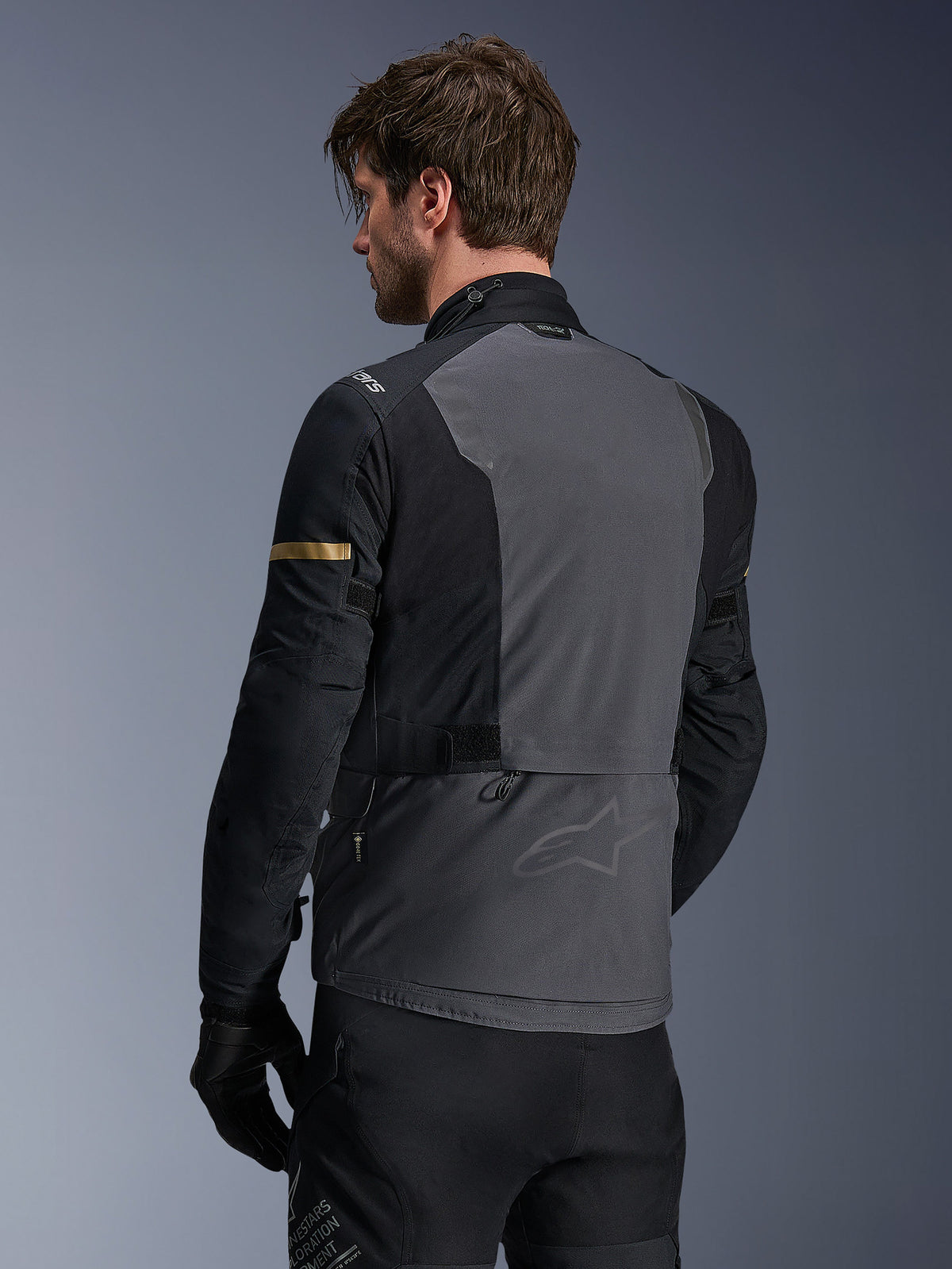 Alpinestars ST-7 2L GORE-TEX Jacket, Motorcycle Jacket, Deep Gray Black and Dark Khaki, rear view showing large gray back panel with subtle branding, black sleeves with gold-toned khaki accents, adventure-ready waterproof textile design