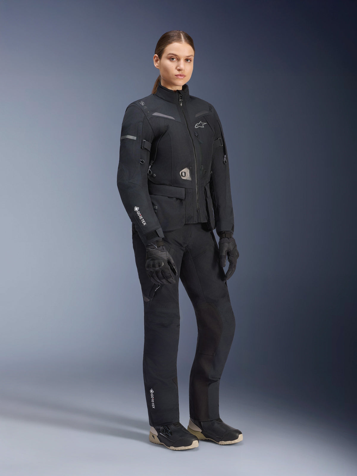 Alpinestars Women Stella ST-7 2L GORE-TEX Jacket, Black, worn with matching motorcycle pants and gloves, adventure road-touring gear with laminated GORE-TEX branding on the sleeve and a tailored women's fit.