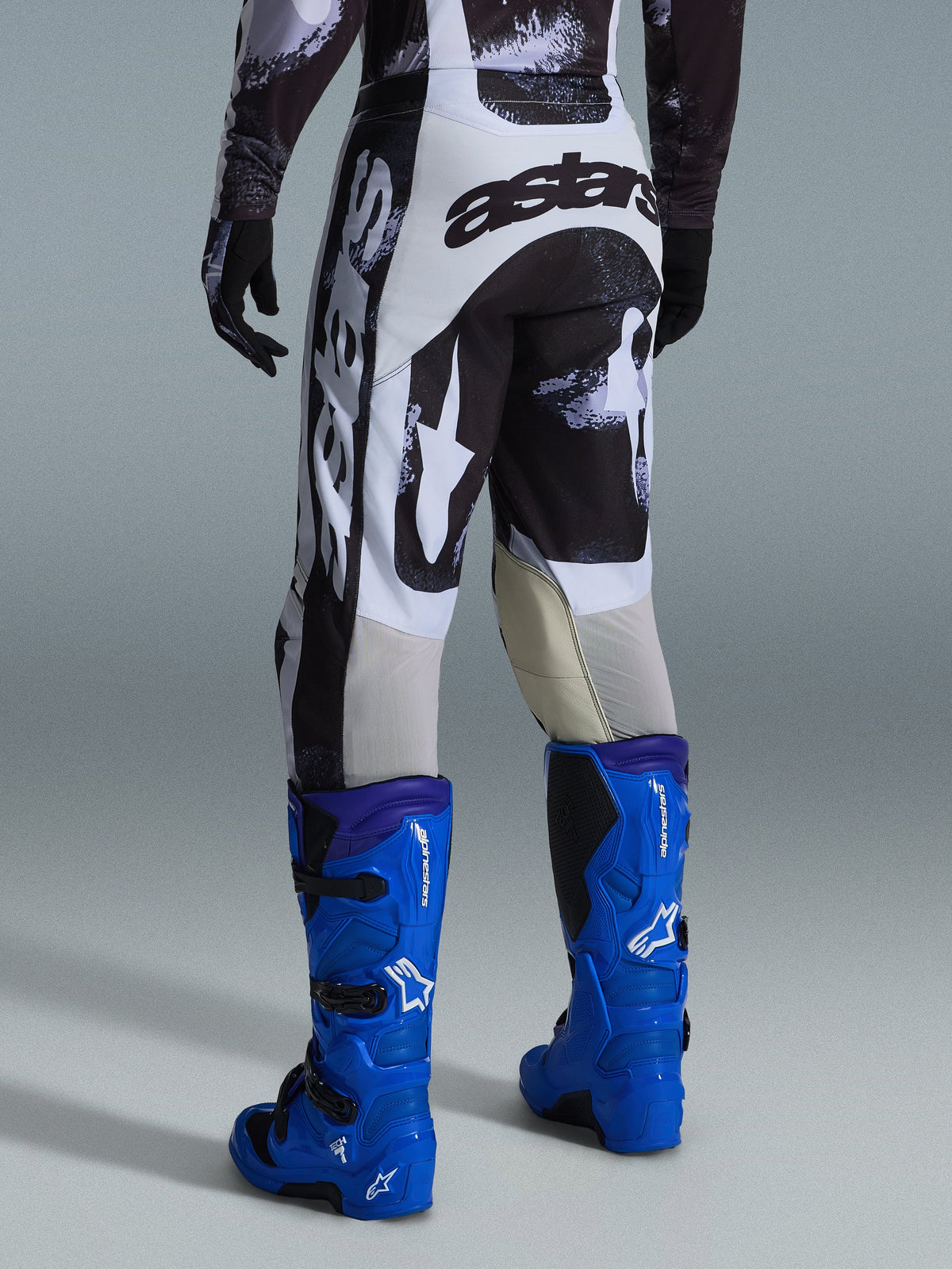 Alpinestars 2026 Racer Lahnd Pants, Motocross Pants, Iron Camo gray and black pattern, back view showing large white and black astars branding, paired with bright blue motocross boots, professional off-road racing gear