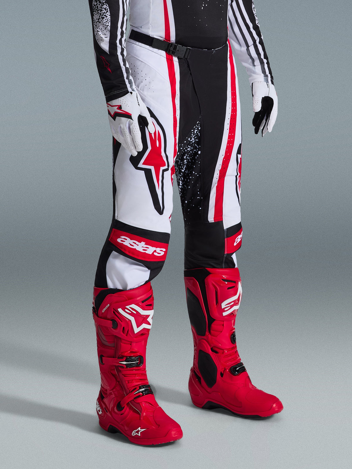 Alpinestars 2026 Techstar Nomur Pants, Motocross Pants, Black White Red, worn with vibrant red racing boots and white gloves, featuring bold vertical stripes, a large red star logo on the thigh, and reinforced knee panels for off-road performance.