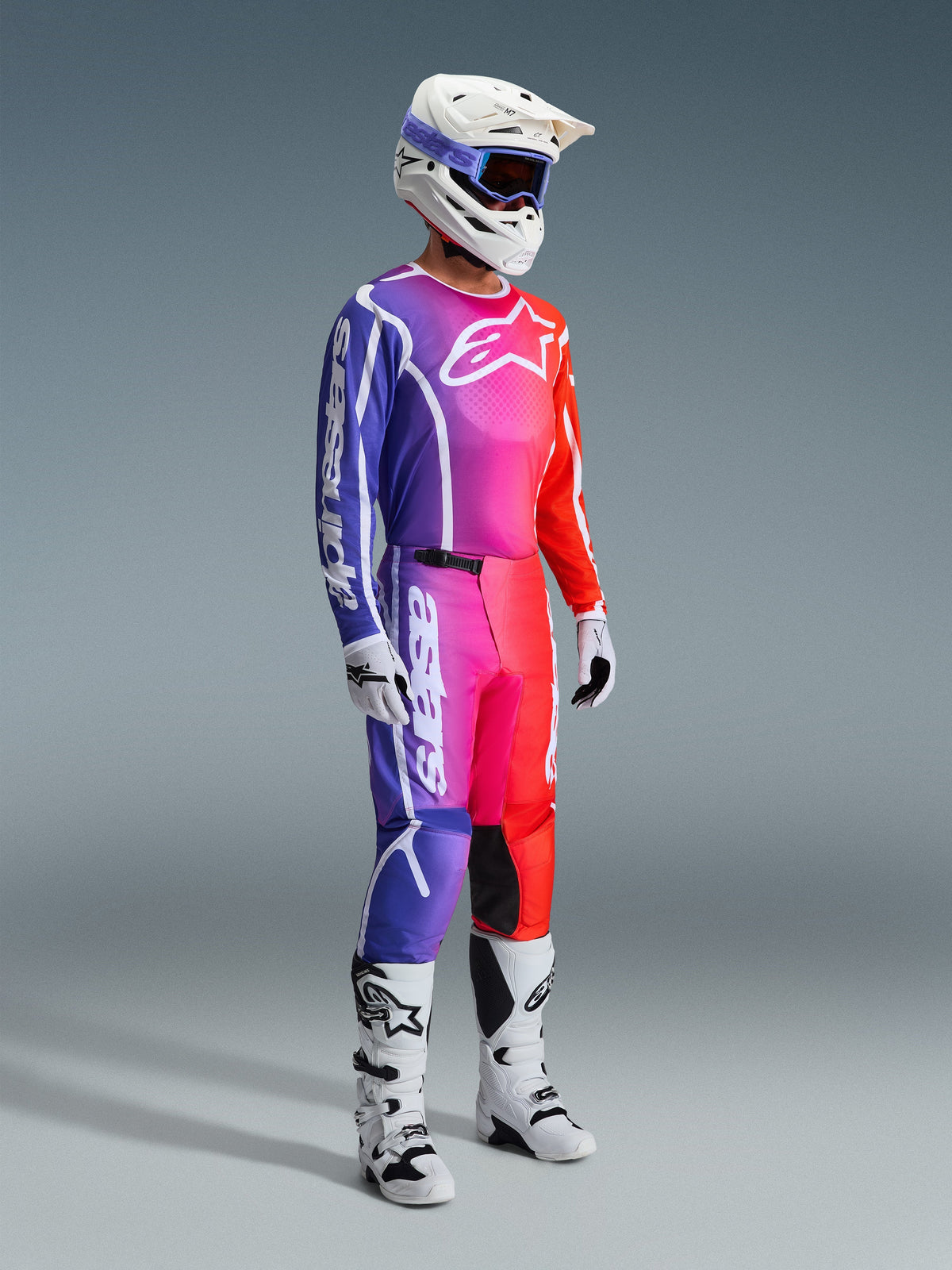 Alpinestars 2026 Fluid Apex Pants, Motocross Pants, Multicolor gradient of purple, pink, and orange, worn with matching jersey, white helmet, and white boots, featuring bold white branding and ergonomic design for off-road racing