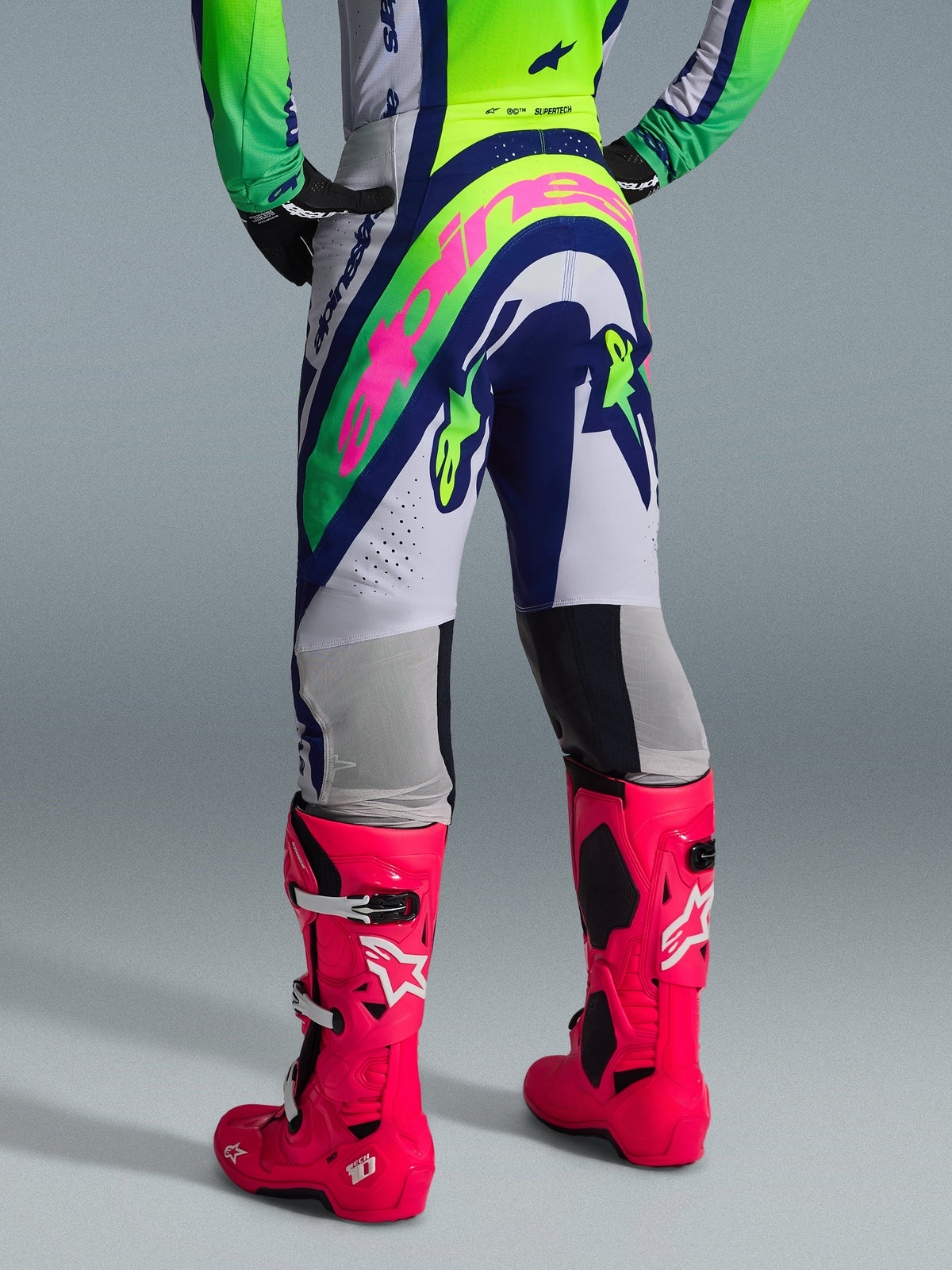 Alpinestars 2026 Supertech Vista Pants, Motocross Pants, Light Gray Yellow Fluo and Blue, rear view featuring a large pink Alpinestars logo, worn with matching racing jersey and bright pink Tech 10 boots, professional off-road gear