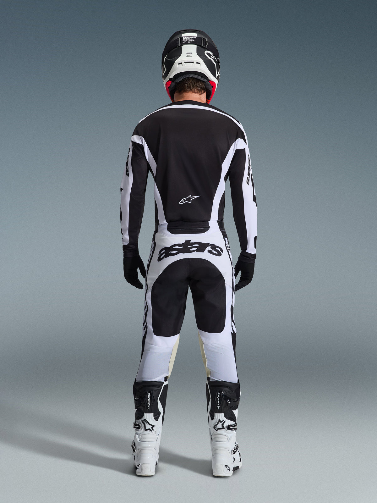 Motocross rider from the back wearing complete racing gear, 2026 Racer Riway Jersey in White and Black, matching pants with 'astars' branding on the seat, black helmet with white details, black gloves, and white and black boots, coordinated professional off-road outfit