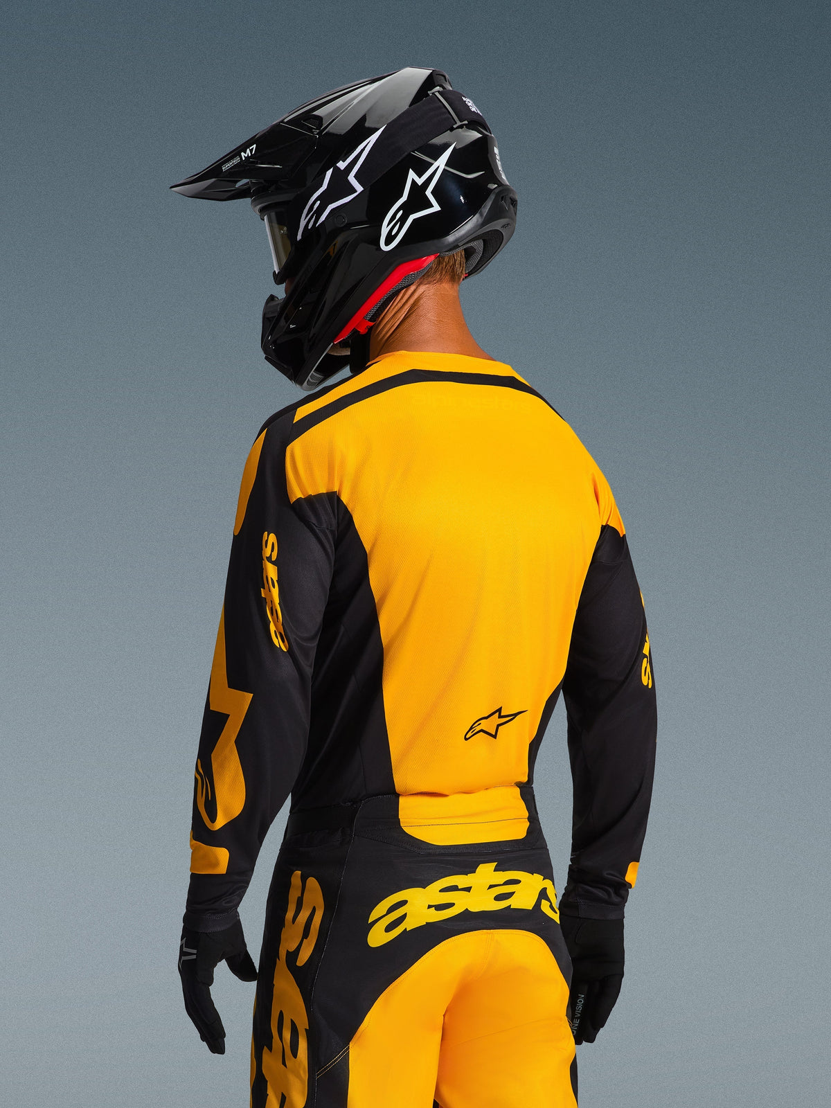 Rear view of a motocross rider wearing the Alpinestars 2026 Racer Riway Jersey in Yellow and Black, featuring a bold yellow back panel and black sleeves with yellow branding, paired with matching motocross pants and a black helmet for a complete off-road racing kit.