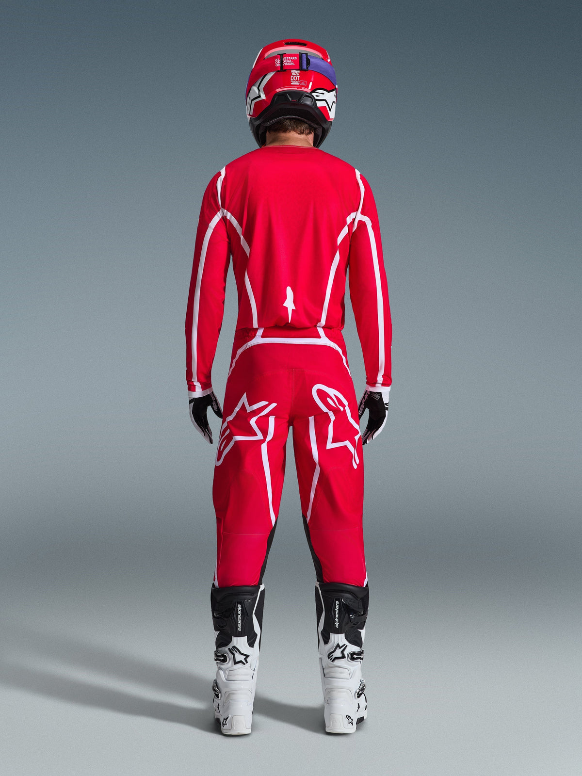 Motocross rider viewed from behind wearing the Alpinestars 2026 Fluid Apex Jersey in Red and White, matching red pants with prominent white star logos, a red helmet, white and black motocross boots, and black and white gloves, complete kit for off-road racing