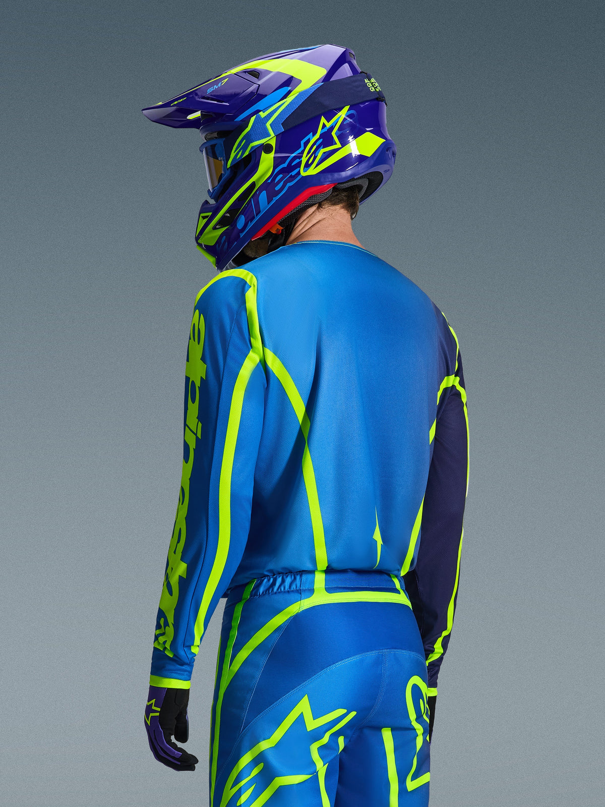 Alpinestars 2026 Fluid Apex Jersey, Blue Yellow Fluo, back view of rider wearing matching motocross pants and helmet, featuring fluorescent yellow geometric graphics and a relaxed athletic fit, coordinated off-road racing gear