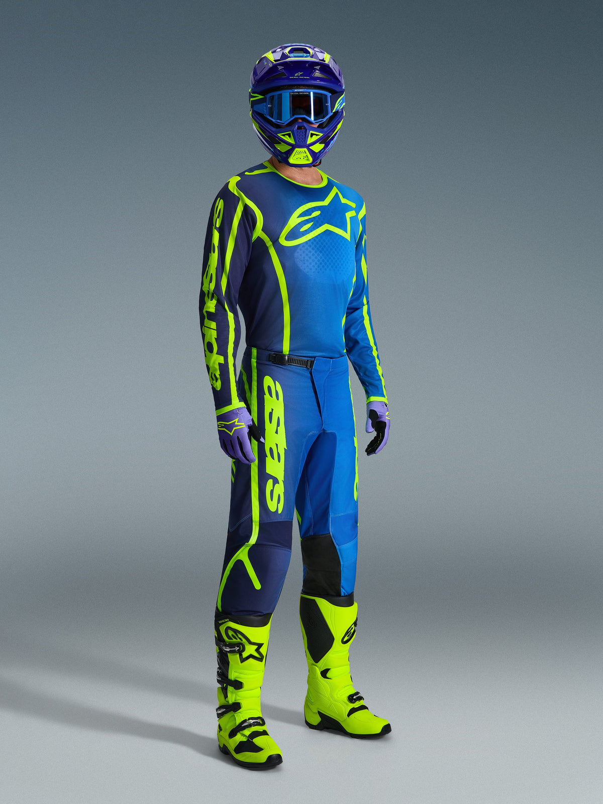 Alpinestars 2026 Fluid Apex Jersey, Blue and Yellow Fluo, worn by a model in a complete motocross gear set including matching pants, a purple and yellow helmet, and bright yellow fluo boots.