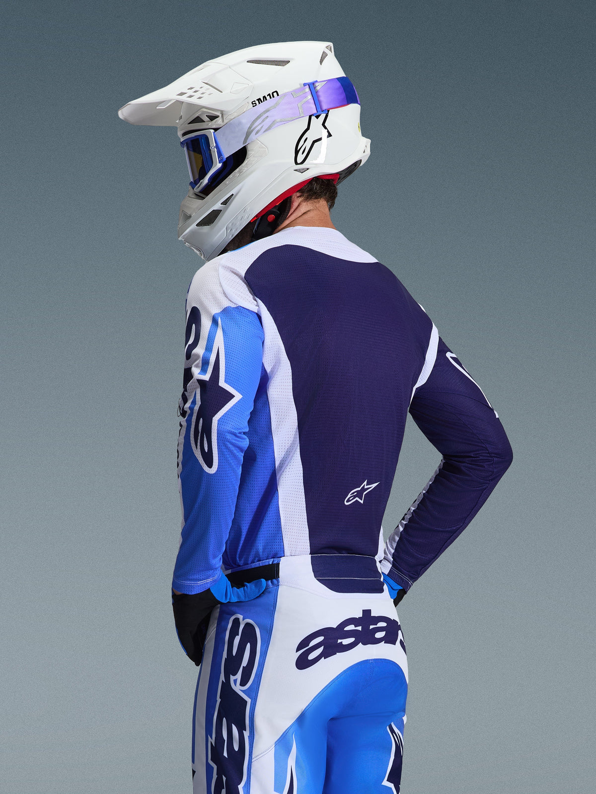 Motocross rider wearing the Alpinestars 2026 Racer Air Portl Jersey in Ucla Blue and White, rear view highlighting the breathable navy blue mesh back panel, worn with matching pants and a white Alpinestars helmet with blue goggles, coordinated motocross gear set.