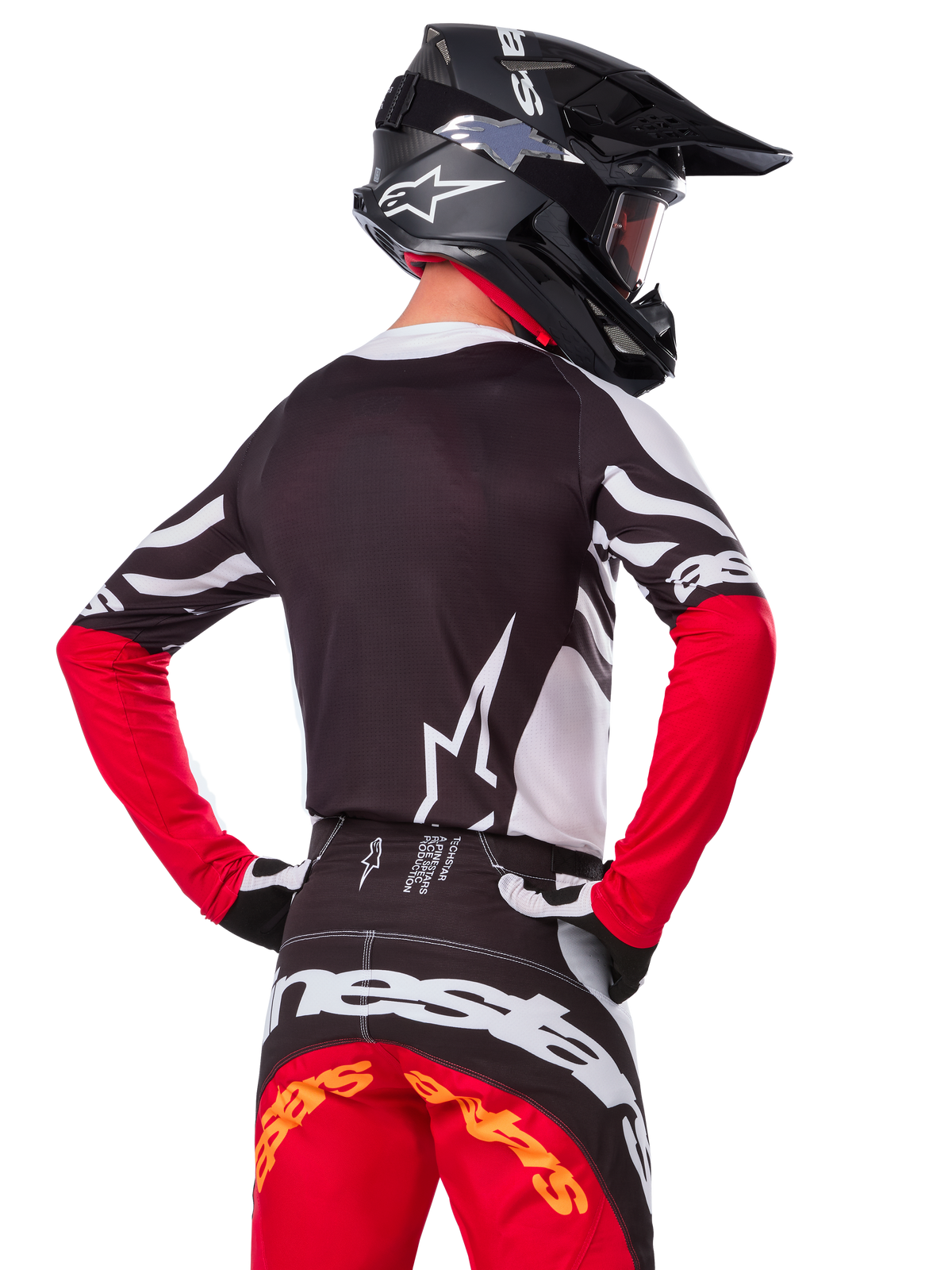 Motocross rider from the back wearing the Alpinestars Limited Edition Techstar Deep Jersey, Black White and High Red, with matching racing pants and a black helmet, athletic fit for off-road performance