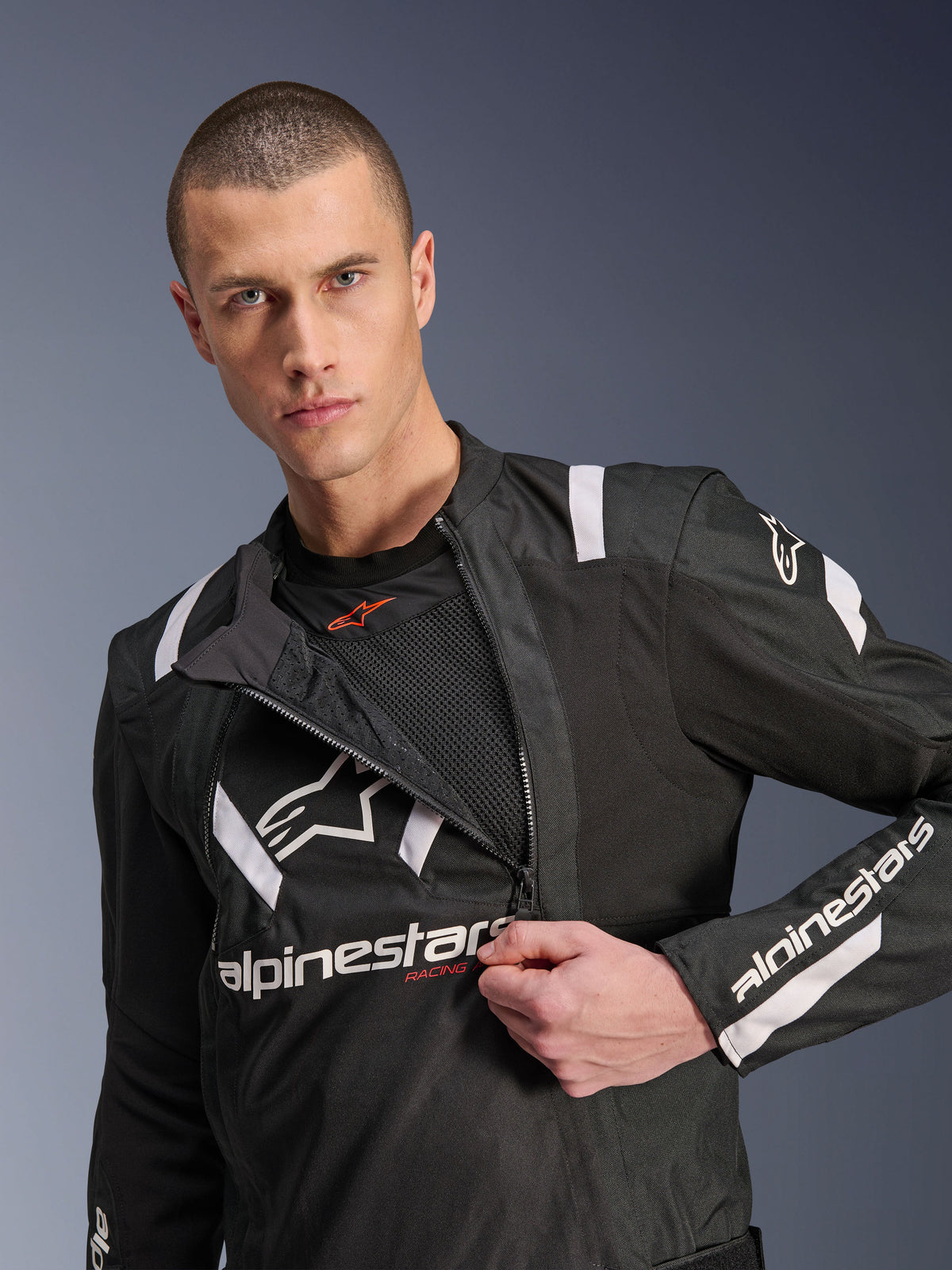 Alpinestars T-Stunt Air Jacket, Black and White motorcycle jacket, male model showing partially unzipped modular front panel revealing mesh airflow layers, white Alpinestars logos on chest and sleeves, sporty design for road riding