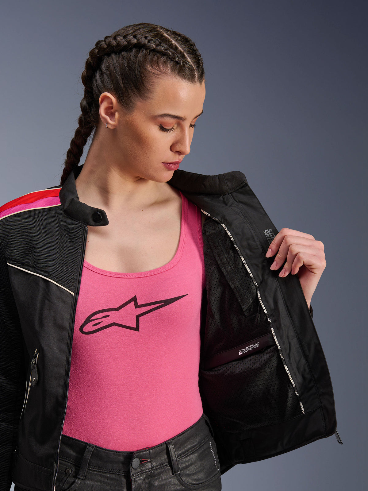 Female rider wearing the Alpinestars Stella T-Dyno Air Jacket in Black Bright Red Fuchsia, shown partially open to reveal the internal waterproof compartment, worn over a pink logo tank top, highlighting the breathable mesh panels and tailored biker fit.