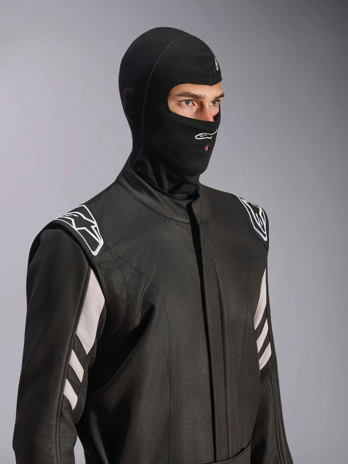 Alpinestars ZX Evo V3 Balaclava, Black, fire-resistant head sock for auto racing, worn by a model in a black racing suit with white accents, features Alpinestars logo on chin, hydration tube access port, professional motorsport protective gear