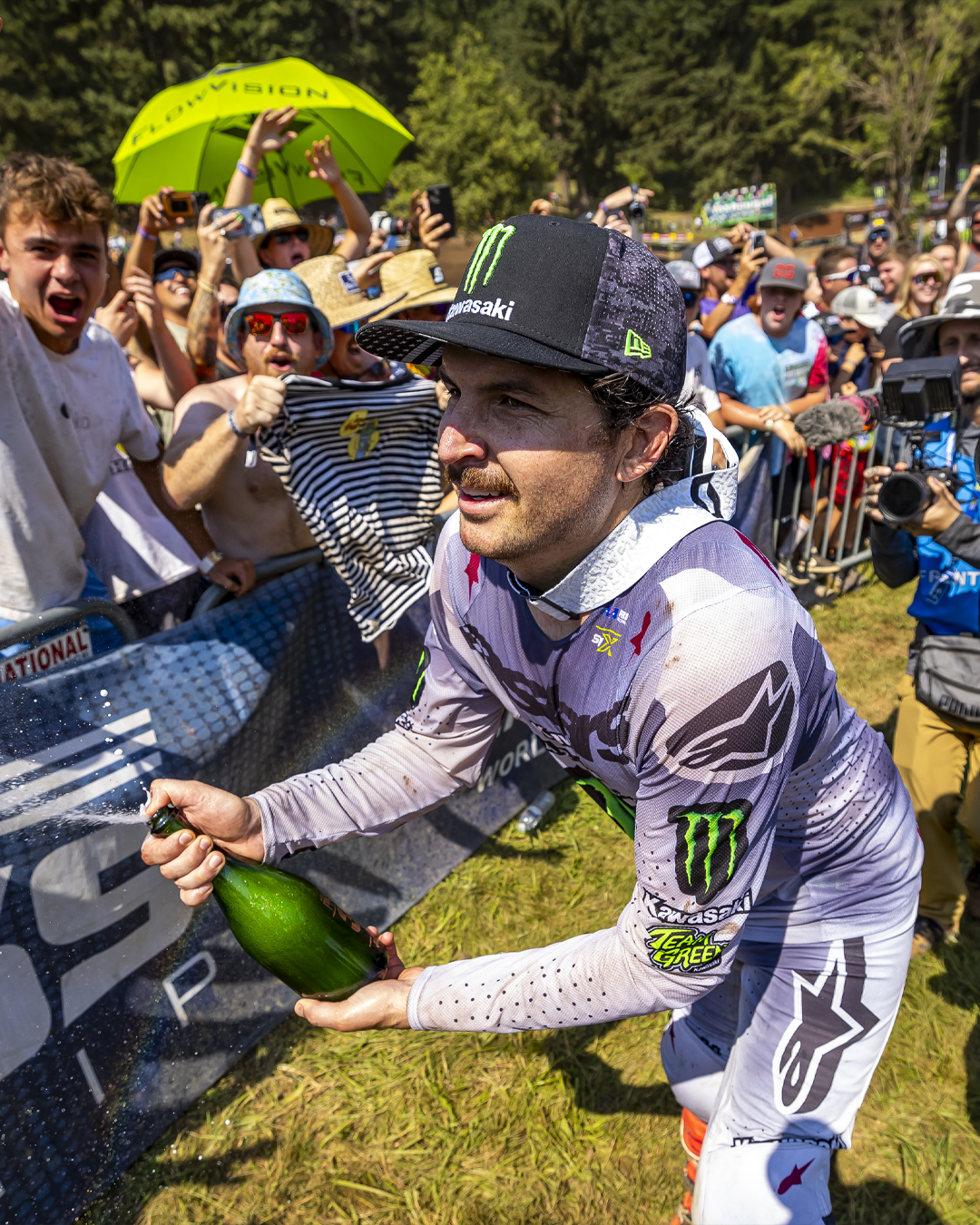 Jason Anderson wearing Alpinestars mx apparel celebrating with a bottle of champagne in front of a crowd after a motocross race.