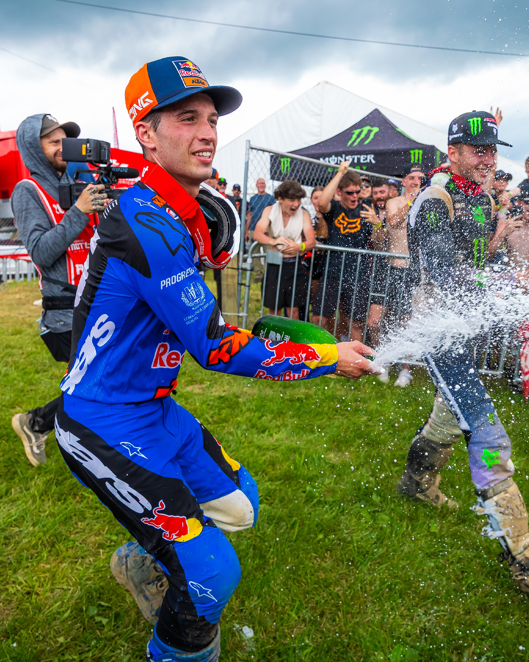 Tom Vialle celebrating with champagne on a grassy track, surrounded by spectators and event branding.