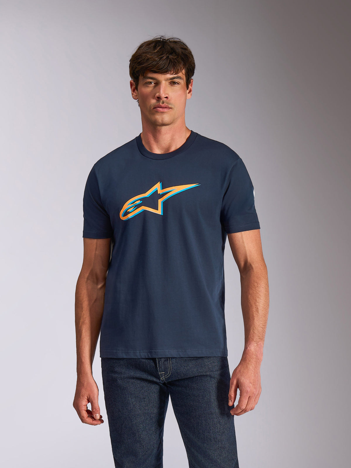 Alpinestars Ageless Shadow CSF Tee, Short Sleeve T-Shirt, Navy Blue with Orange and light blue shadow logo graphic, worn by a model with dark jeans, casual motorsport streetwear