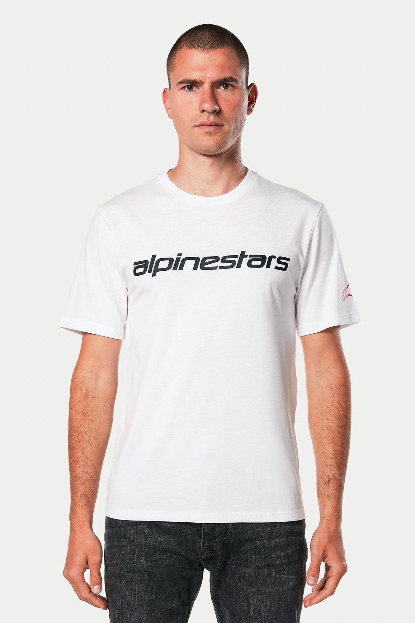 Alpinestars Linear Wordmark 2.0 CSF Tee, Short Sleeve T-Shirt, White with Black linear wordmark on chest and red logo on sleeve, worn by model with dark jeans, casual motorsport streetwear
