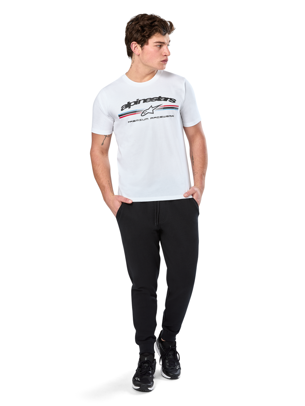Alpinestars Prevail CSF Tee, Short Sleeve T-Shirt, White, featuring a front paddock-style tri-color stripe logo with Alpinestars branding, worn by a model with black joggers and black sneakers, casual motorsport streetwear