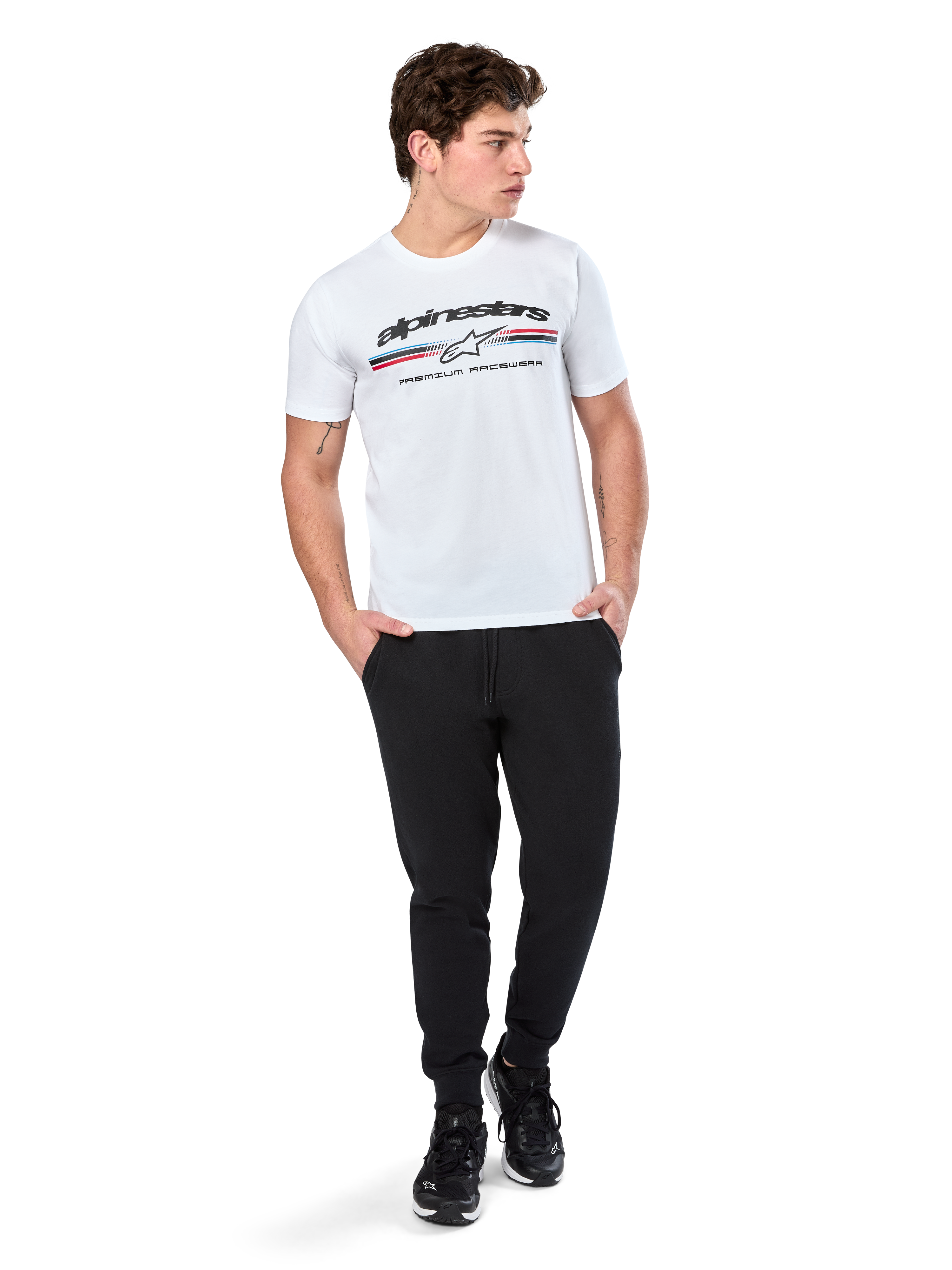 Alpinestars Prevail CSF Tee, Short Sleeve T-Shirt, White, featuring a front paddock-style tri-color stripe logo with Alpinestars branding, worn by a model with black joggers and black sneakers, casual motorsport streetwear