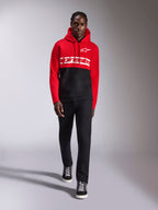 Alpinestars Parallel Hoodie, color-blocked pullover fleece, Red and Black, featuring white Alpinestars word logo across the chest and Astars logo on the left chest, worn by a model with black pants and high-top sneakers, casual motorsport streetwear