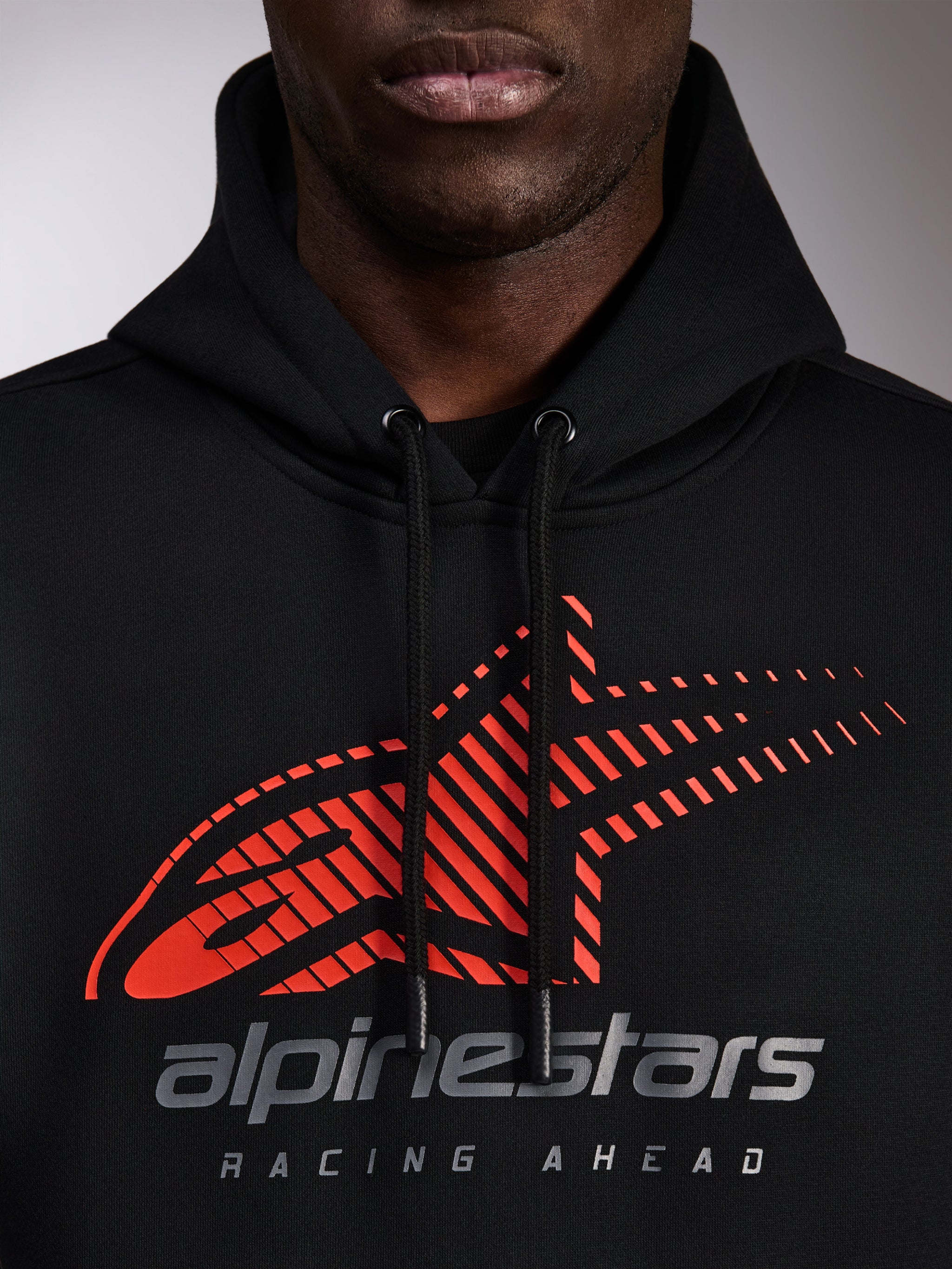 Alpinestars Pulse Hoodie, black pullover hoodie, close-up of chest featuring red Astars logo with speed line fade and silver branding, black drawstrings with dipped tips, casual motorsport streetwear