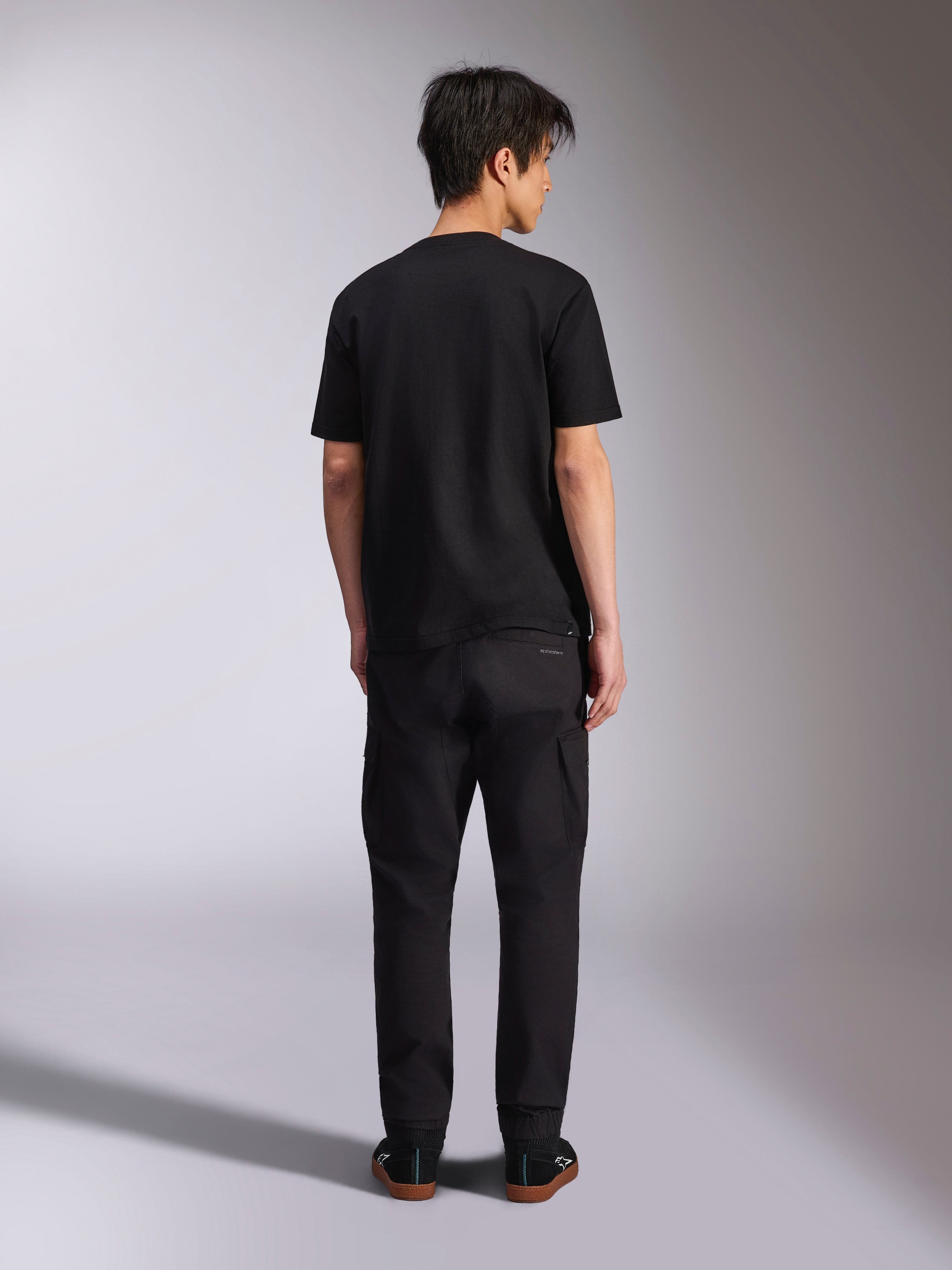 Alpinestars Noka CSF Tee, Short Sleeve T-Shirt, Black, back view of model wearing the tee with black pants and sneakers, casual motorsport streetwear style