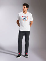 Alpinestars Plate CSF Tee, Short Sleeve T-Shirt, White, featuring a front Astars MX plate graphic with orange and blue accents, worn by a model with black pants and sneakers, Casual Motorsport Streetwear