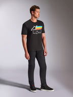 Alpinestars Trifecta CSF Tee, Short Sleeve T-Shirt, Black, white Astars logo with blue, yellow, and orange stripes and 'Racing Ahead' graphic, worn by a model with black pants and sneakers, casual motorsport-inspired lifestyle apparel