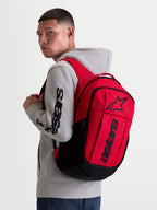 Alpinestars GFX Boss Backpack, 20L Urban Sportswear Daypack, Red and Black, shown on model wearing a grey hoodie. Featuring durable 600D polyester construction, raised silicone Astars graphic branding, and internal laptop sleeve. Ideal for daily commuting and everyday carry.