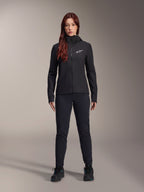 Woman wearing Alpinestars Stella A-Dura Thermal Jacket, Black, lightweight insulated cycling jacket with hood and white Astars logo on the chest, paired with black pants and athletic shoes