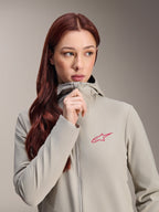 Alpinestars Woman Stella A-Dura Thermal Jacket, Titanium gray with a pink Alpinestars star logo, model with long red hair wearing and zipping up the hooded jacket, lightweight insulated cycling apparel for cold weather.