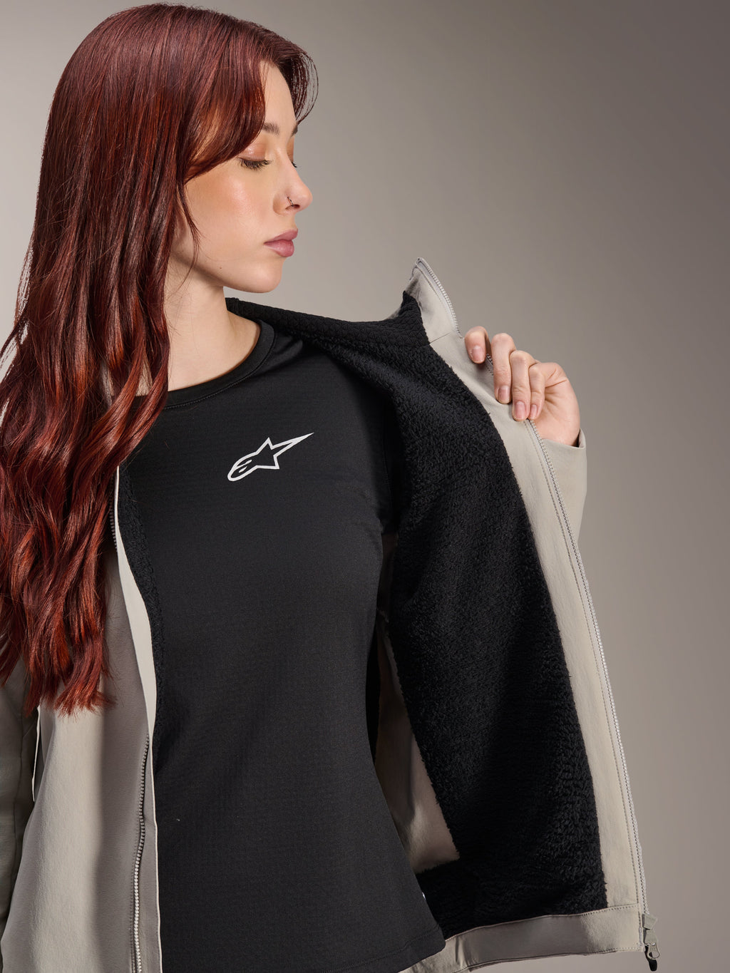 Woman wearing the Alpinestars Stella A-Dura Thermal Jacket in Titanium, showcasing the black textured fleece lining, worn over a black t-shirt with a white star logo, lightweight mountain bike jacket for cold conditions.