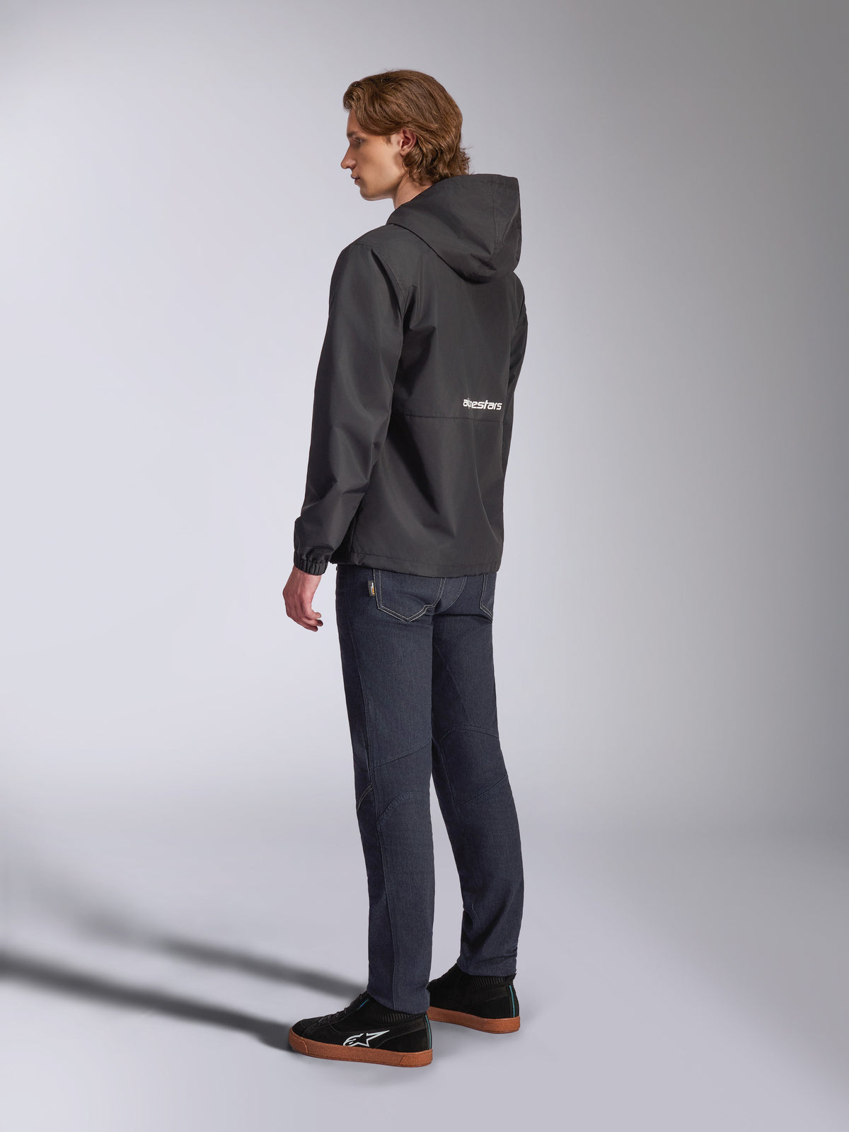 Alpinestars Speeder Chromium Windbreak Jacket, Black with white logo on the back, men's casual windbreaker with hood, side profile view worn with dark jeans and black sneakers, motorsport-inspired streetwear