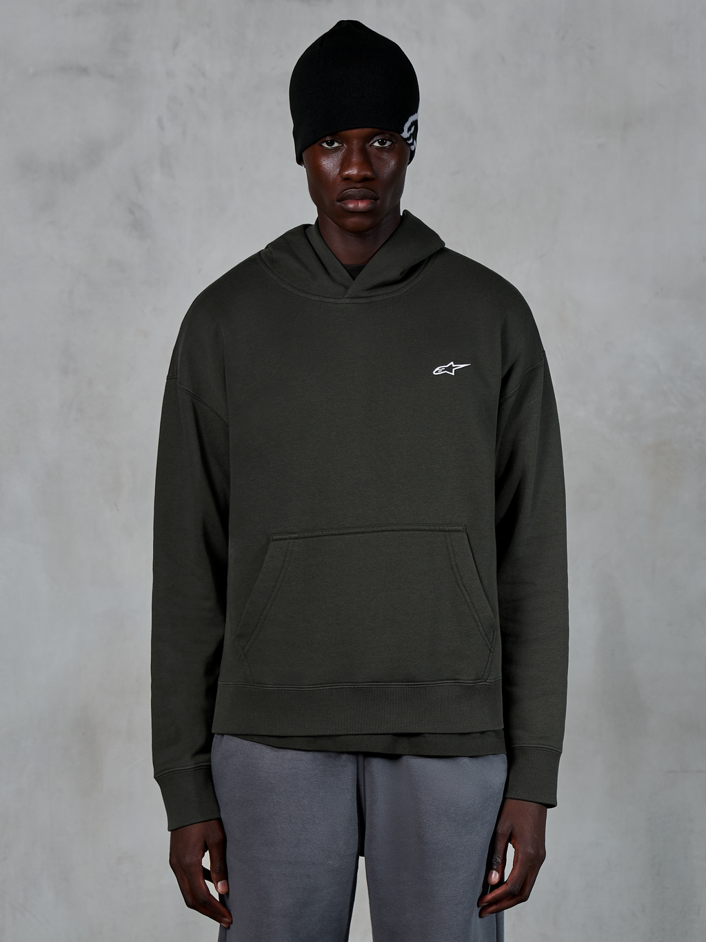 Alpinestars Essentials Ageless Hoodie, casual streetwear, Off Black pullover with a small white Alpinestars logo on the chest, worn with a black beanie, minimalist design with a front pouch pocket and stone-wash finish