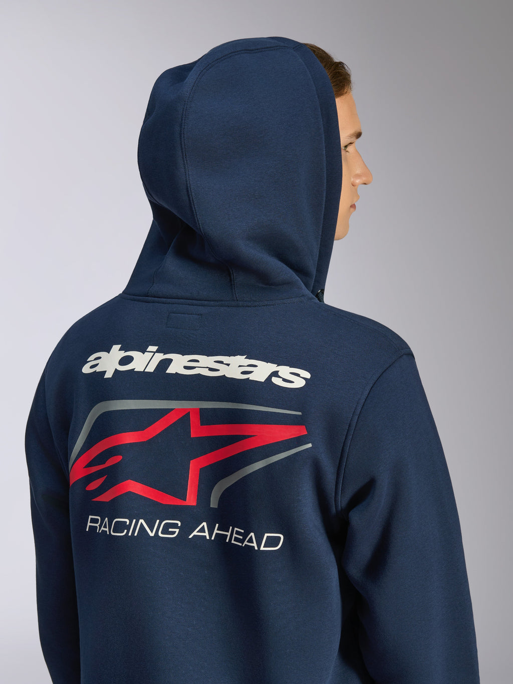 Alpinestars Formulation Hoodie, navy blue zip-front fleece, rear view showing hood up and large back graphic with white Alpinestars wordmark, red star logo, and 'RACING AHEAD' text, casual motorsport streetwear