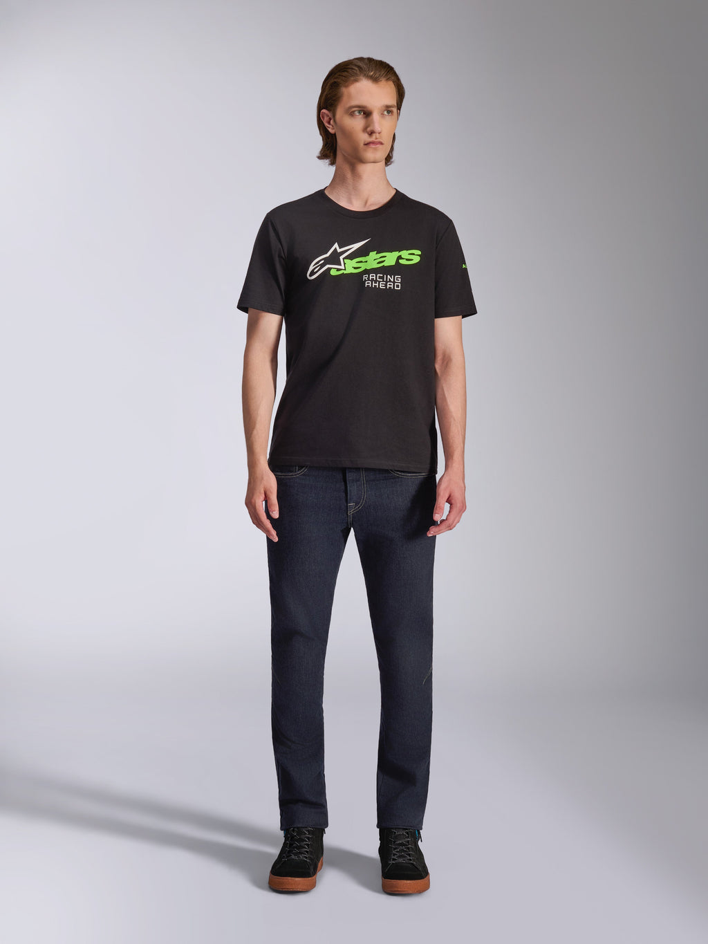 Alpinestars Entitled CSF Tee, Short Sleeve T-Shirt, Black, featuring a white star logo, neon green 'stars' text, and 'Racing Ahead' graphic on the chest, worn by a model with dark jeans, casual motorsport-inspired apparel