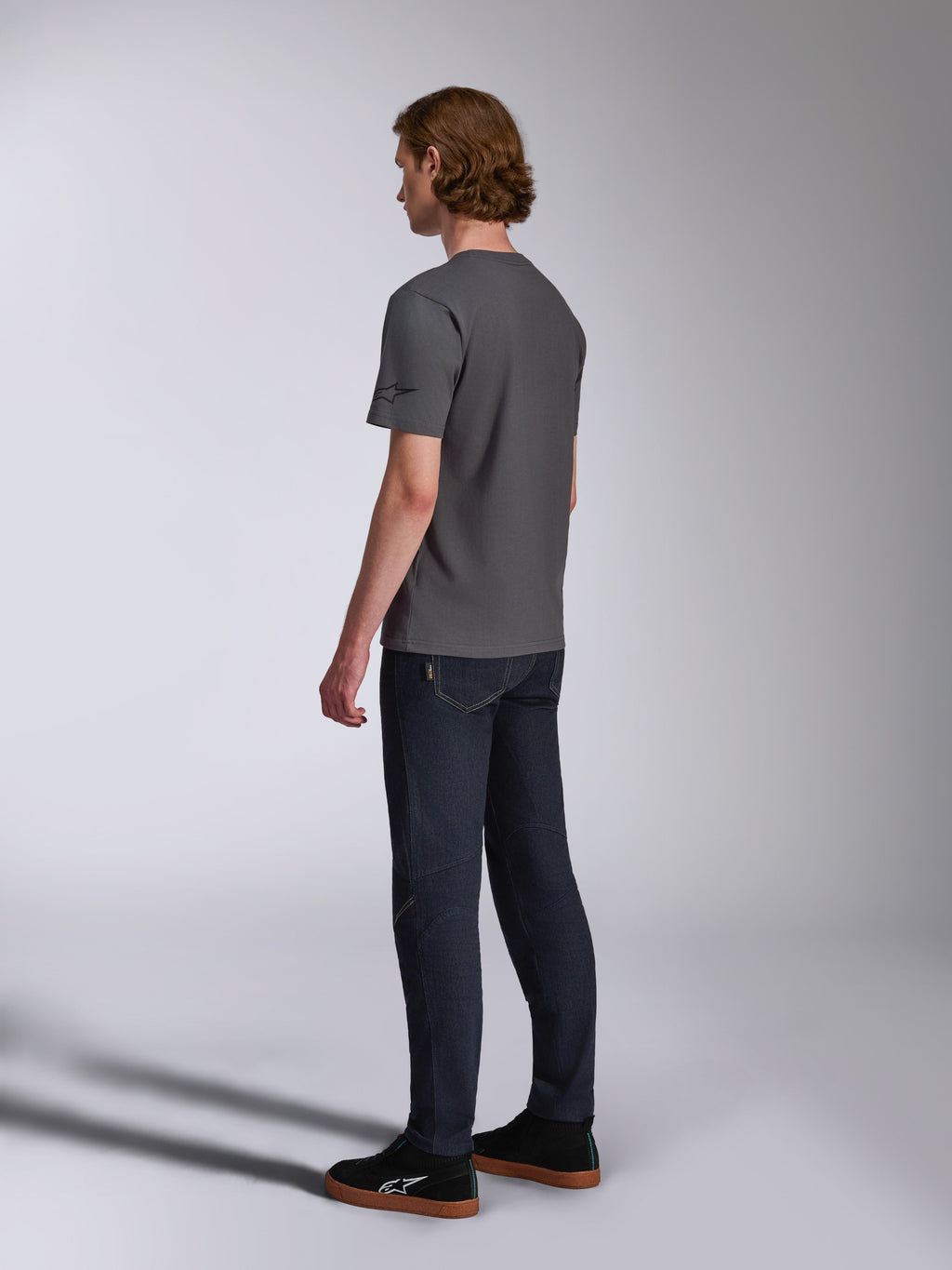 Alpinestars Waving CSF Tee, Short Sleeve T-Shirt, Charcoal, back-side view on model, small black star logo on sleeve, worn with dark denim jeans and black sneakers, casual motorsport streetwear