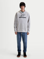 Alpinestars Prelude Oversized Hoodie, Men's Sportswear Fleece Pullover in Cement Gray. Features a relaxed fit with a black puff-print logo on the chest, a kangaroo pocket, and adjustable hood, shown on model with blue jeans.