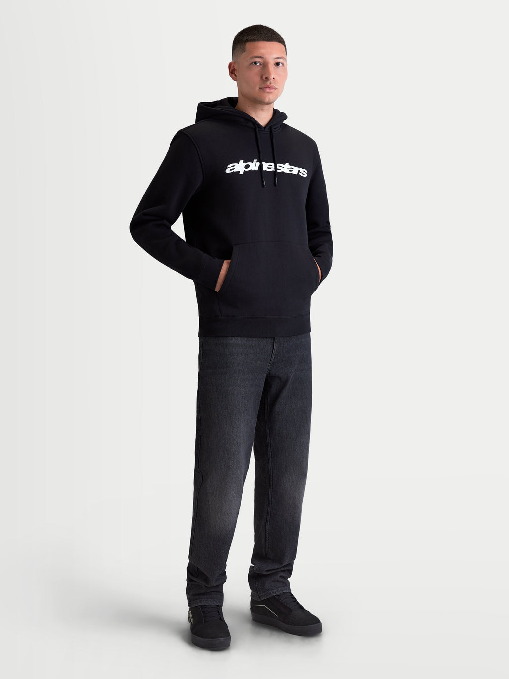 Alpinestars Race Wordmark Hoodie, Men's Sportswear Pullover Fleece, Black and White, featuring a bold white linear chest logo, self-lined hood with drawstrings, and a front pouch pocket. Constructed from a comfortable cotton and recycled polyester blend for everyday casual wear, shown on model.