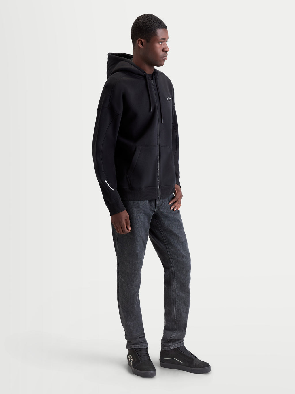 Alpinestars Entity Oversized Hoodie, Sportswear Zip-Front Fleece, Black, 80% Cotton and 20% Recycled Polyester. Features include a Vislon front zipper, kangaroo pocket, and embroidered logo on the chest and sleeve. Shown on model for a relaxed, oversized fit, ideal for casual motorsport style.