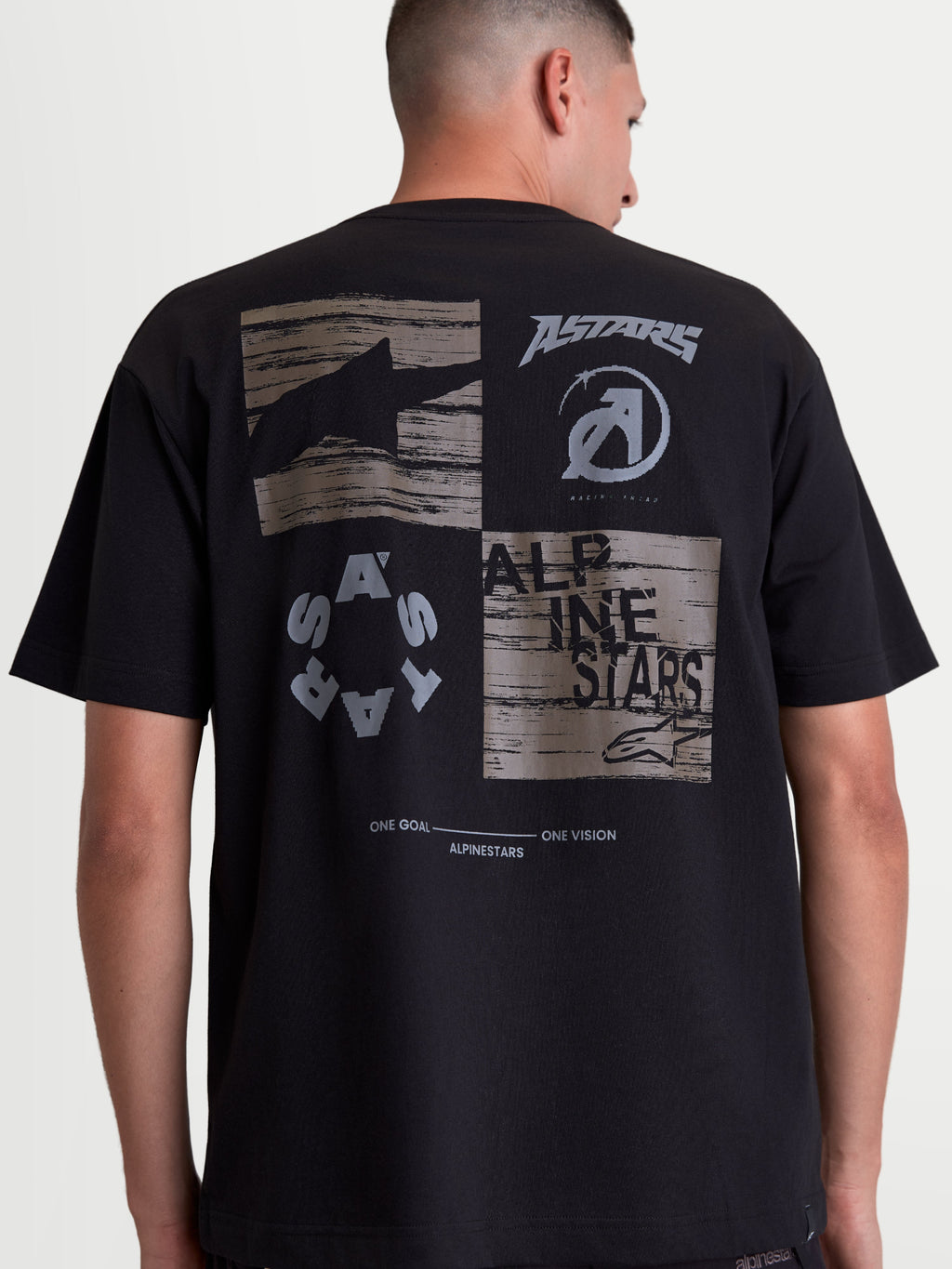 Alpinestars Checkback Oversized CSF Tee, Black Sportswear T-Shirt, back view on model showing a large grey graphic with Astars logos, Alpinestars text, and 'One Goal One Vision' slogan. Oversized fit, soft-hand print, cotton-polyester blend.