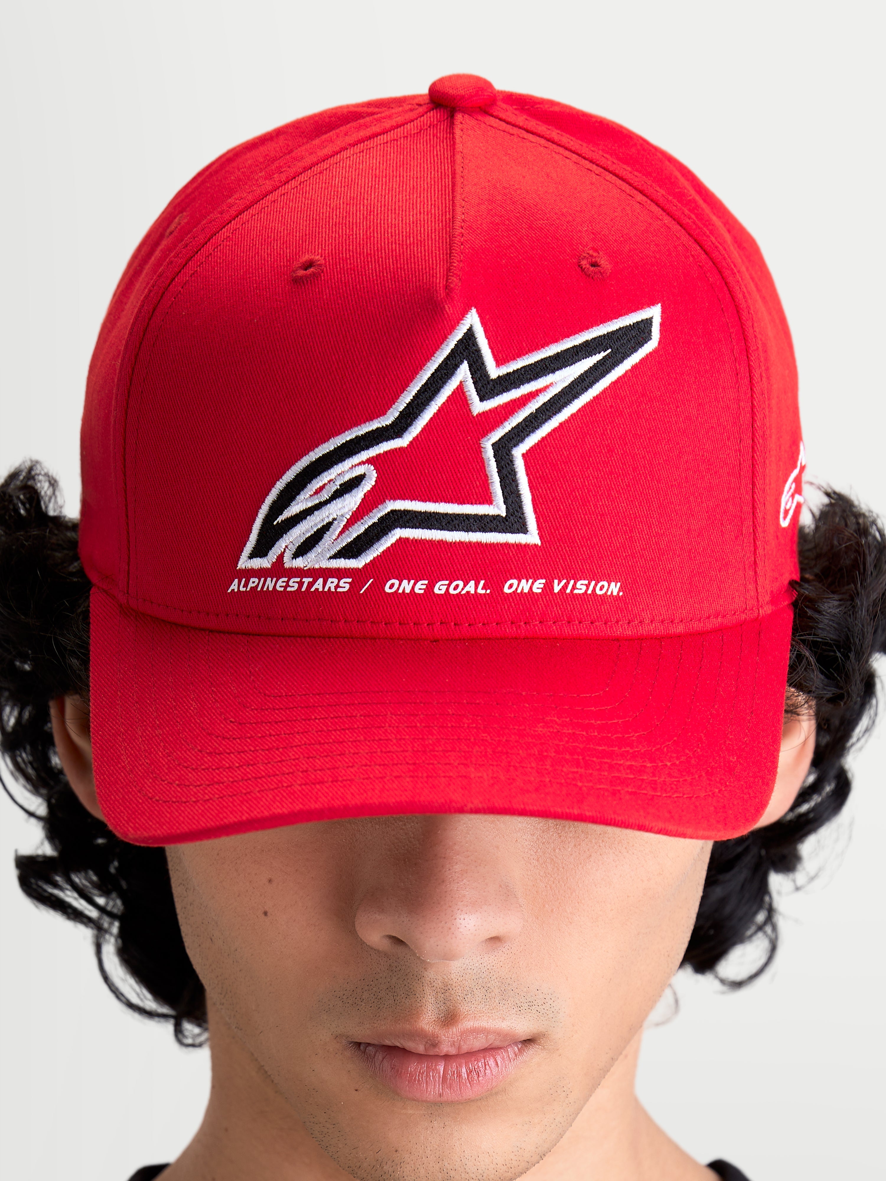 Alpinestars Lineout Hat, Red Sportswear Baseball Cap, on-model front view with a structured crown and curved bill. Features a large embroidered Astars logo in white and black with the brand motto 'ONE GOAL. ONE VISION.' underneath. Casual and performance-inspired red textile headwear for motorsports enthusiasts.