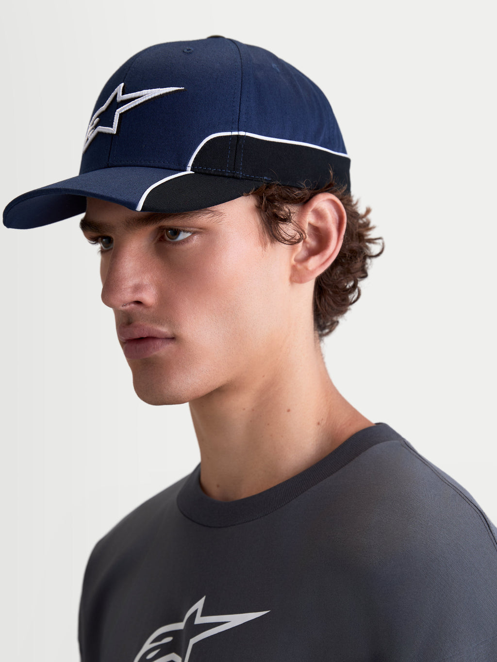 Alpinestars 500 Snapback Hat, Sportswear Baseball Cap, Unisex, Navy Blue and Black, Durable Cotton Twill, features curved bill and 3D Astars logo embroidery with white contrast piping, on-model side view.