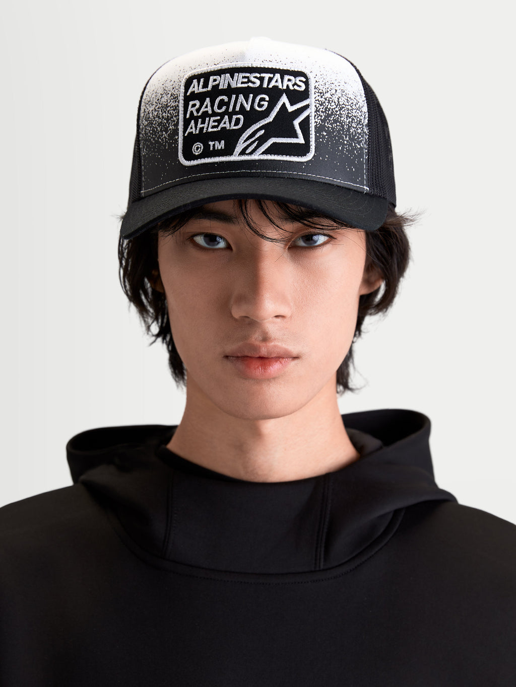 Alpinestars Gravel Trucker Hat, Sportswear Lifestyle Cap, Black and White, On-Model Front View featuring a Curved Bill, Breathable Mesh Back, and Racing Ahead Woven Patch with Gravel Texture Detailing.
