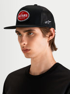 Alpinestars Hotlink Trucker Hat, motorsport-inspired flat bill snapback cap worn by a model, black and red, featuring a structured crown and front Astars logo patch with bike chain border