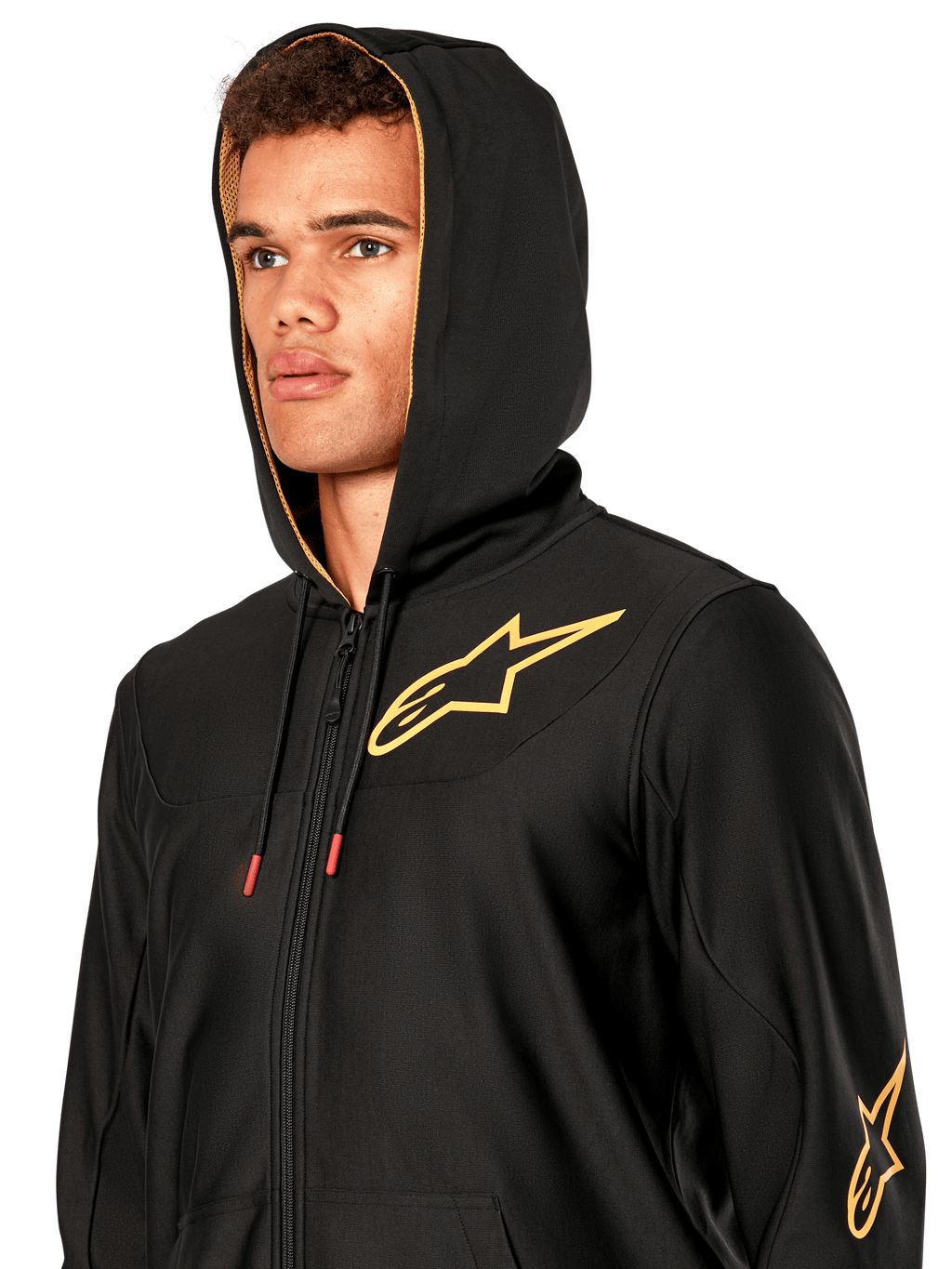 Man wearing Alpinestars Sessions V3 Hoodie, black zip-front fleece with gold star logo on chest, gold mesh-lined hood with tech drawcords, casual motorsport streetwear